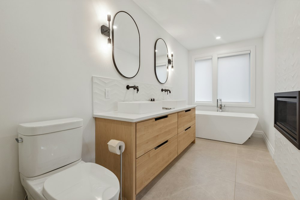 Baño con mueble de madera, dos lavabos, espejos ovalados y bañera