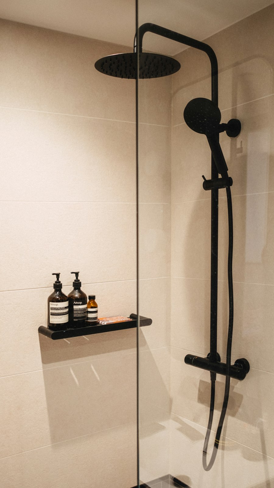Ducha con azulejo beige, grifería negra y repisa